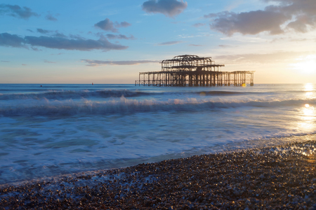 Abandoned West pier in Brighton at sunset, warm blue and red colors. Pebbles glittering in the foregroundのeditorial素材