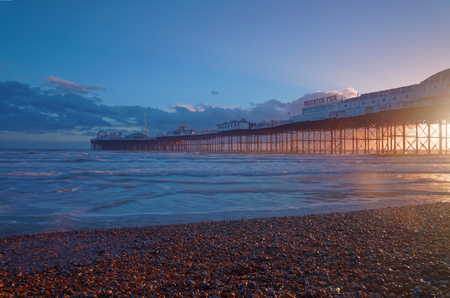 Brighton pier at sunset, warm red and blue colors. Pebbles in the foregroundのeditorial素材