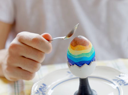 Closeup of a the hand of a man in white shirt starting to eat a painted colorful Eastern egg with a...