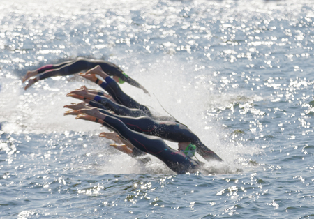 STOCKHOLM - AUG 26, 2017: Legs of the female competitors wearing green bathing cap jump into the glittering water after the start signal in the Women's ITU World Triathlon series event August 22, 2017 in Stockholm, Swedenのeditorial素材
