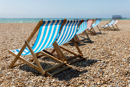 Classic blue, red and white striped empty deckchairs on the beach. The old pier in Brighton in the backgroundの写真素材