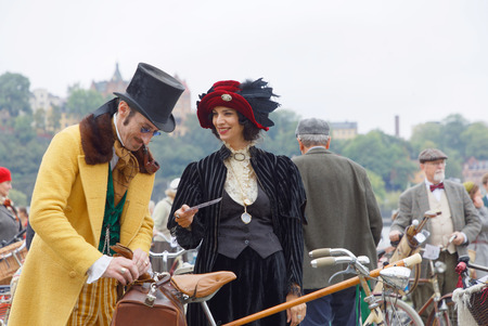 STOCKHOLM - SEPT 23, 2017: Elegant upper class lady and gentleman with bicycles dressed in yellow and black clothes, cylinder hat and feather hat from aprox 1900 in the Bike in Tweed event September 23, 2017 in Stockholm, Swedenのeditorial素材