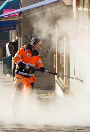 STOCKHOLM, SWEDEN - NOV 07, 2017: Official in orange uniform working to remove graffiti using steem on a wall in central Stockholm, Sweden, November 07, 2017のeditorial素材