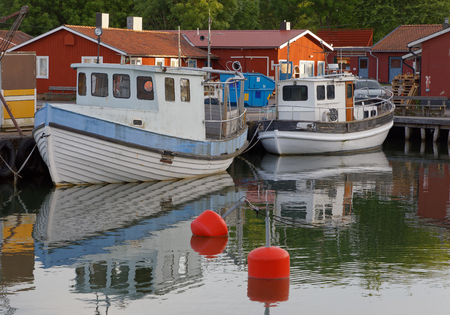 GRISSLEHAMN, SWEDEN - JUL 08, 2017: Morning light and traditional fishing boats in the small harbor, red houses in the background. Grisslehamn Sweden, July 08, 2017のeditorial素材