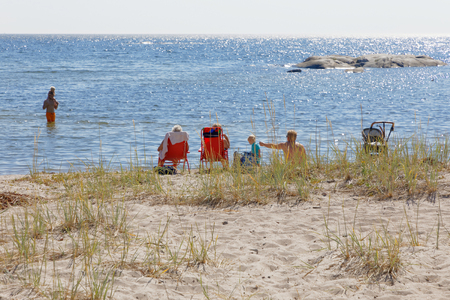 KVARNSAND, SWEDEN - JUL 25, 2018: Sunbathing people relaxing on the beach, glittering blue water in Kvarnsand, Sweden, July 25, 2018のeditorial素材
