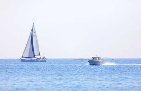 GRISSLEHAMN, SWEDEN - JUL 18, 2018: One sailship and one motor boat on the blue ocean in the swedish archipelago, islets in the background. July 18 2018, Grisslehamn, Swedenの写真素材
