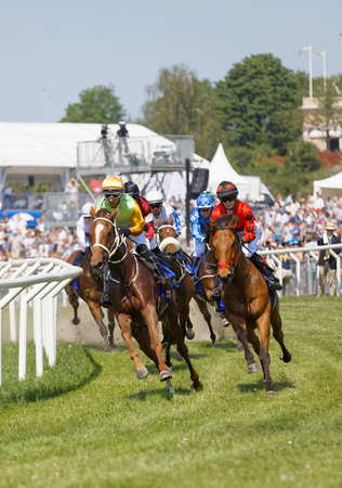 STOCKHOLM, SWEDEN - JUNE 06, 2019: Tough fight between many colorful jockeys riding arabian race horses in a curve and audience in the background at ATG Nationaldags Galoppen at Gardet. June 6, 2019 in Stockholm, Swedenのeditorial素材
