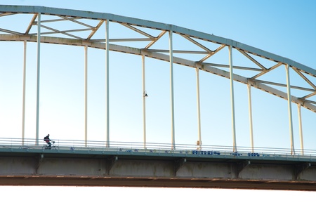 part of an arch bridge with a lonely bicyclist on itの写真素材