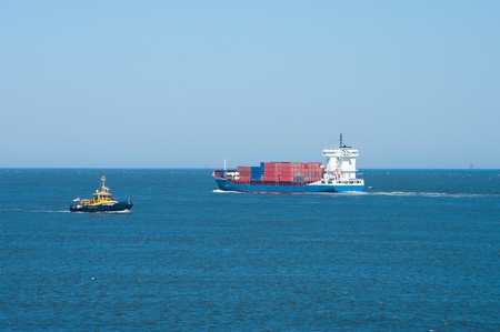 container ship passing a tugboat at the entrance of Rotterdam harborの写真素材