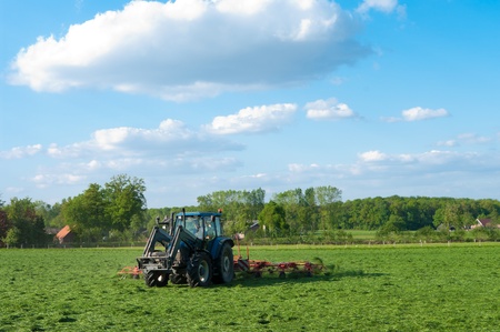 farmer busy with tractor to flip just mowed grassの写真素材
