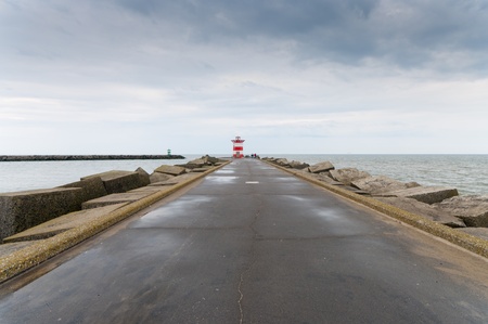 small red lighthouse at the end of a seawallの写真素材