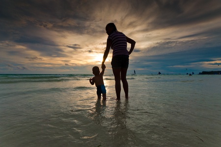 silhouette of a mother with her baby at sunset on a tropical beachの写真素材