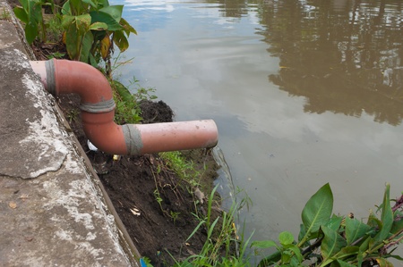 water coming out of a small pipe flowing into a riverの写真素材