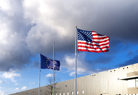 waving american and european flag against a dark cloudy sky