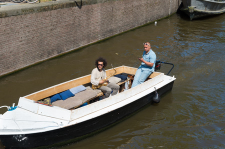 two musicians in a boat on an amsterdam canal. Amsterdam counts 165 canals with a total lenght of 100 km.のeditorial素材