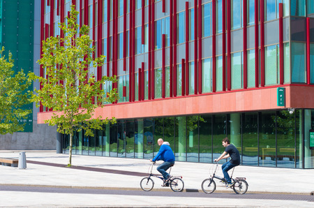 bikers passing a modern office building in Almere, netherlands. It is the youngest and fastest growing city in the country, founded around 1975.のeditorial素材