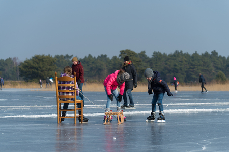 LATTROP, NETHERLANDS - MARCH 3, 2018: Unknown children using a wooden chair and sleigh as their resting point while they are skatingのeditorial素材