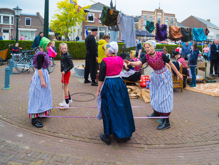 URK, NETHERLANDS - MAY 19, 2018: Unknown girls in traditional costumes playing an old-fashioned string game on the Urkerdays. Urk is on of the best-known fishing villages in the country with the largest fishing fleet.のeditorial素材