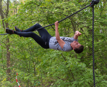 OLDENZAAL, NETHERLANDS - MAY 7, 2017: Unknown athlete hanging on a rope between trees at a survival...