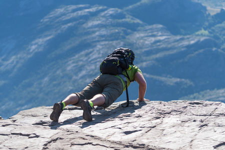 Backpacker looking carefully over the edge of Pulpit Rock. The Pulpit Rock or Preacherâs Chair is a tourist attraction in the municipality of Forsand in Rogaland countyのeditorial素材