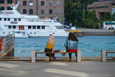 BERGEN, NORWAY - JULY 28, 2018: Two unknown young women sitting on the Bergen pier enjoying the nice viewのeditorial素材