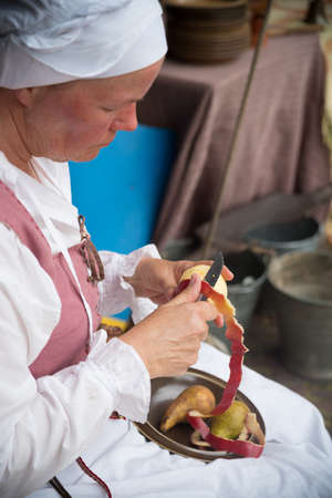 HIERDEN, NETHERLANDS - JUNE 10, 2019: Woman in medieval clothes peeling an apple at a medieval...