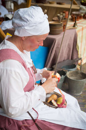 HIERDEN, NETHERLANDS - JUNE 10, 2019: Woman in medieval clothes peeling an apple at a medieval workshopのeditorial素材