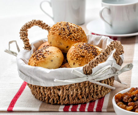 Fresh homemade buns with seeds and raisins in a basket.の写真素材