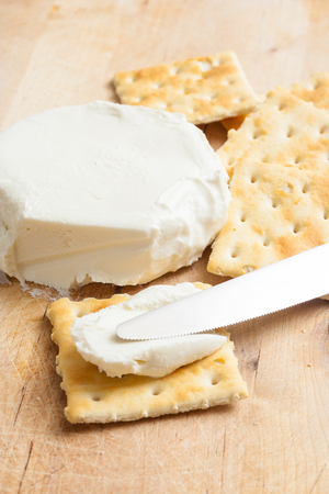 Fresh cream cheese spread with crackers and knife on a wooden cutting board.の写真素材