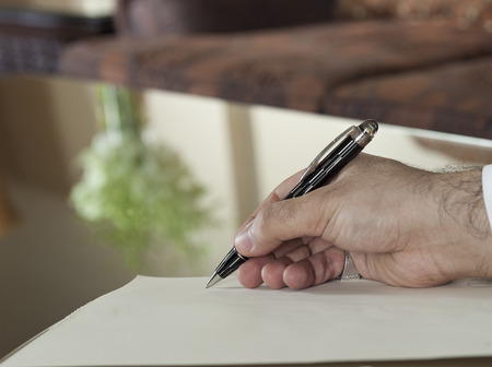 Saudi Arabian Man Hand Writing on A Notebook in a Luxury Home Environment, wearing Saudi Thob, Ghutra and Black Bishtの写真素材