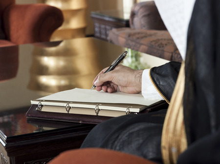 Saudi Arabian Man Hand Writing on A Notebook in a Luxury Home Environment, wearing Saudi Thob, Ghutra and Black Bishtの写真素材