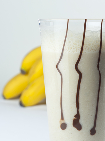 A glass of banana and milk cocktail close up with full fruits in the backgroundの写真素材