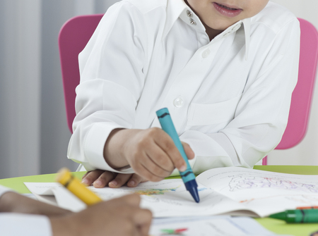 Kids drawing with colored crayons on paper at a tableの写真素材