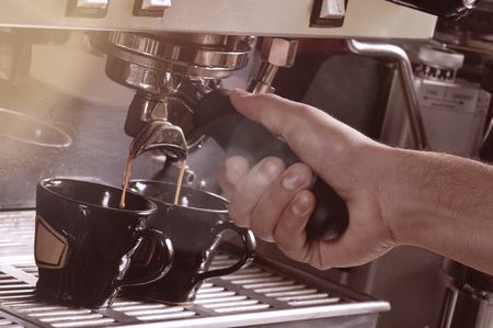 Close up on hands making two cups of espresso coffee on a machineの写真素材