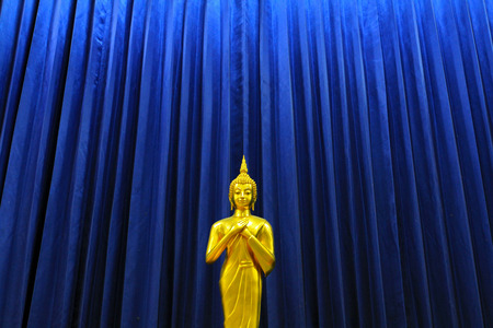Golden Buddha statue with blue curtain backgroundの写真素材