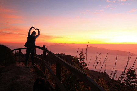 Silhouette of women making heart sign with sunrise and mist background in the morningの写真素材