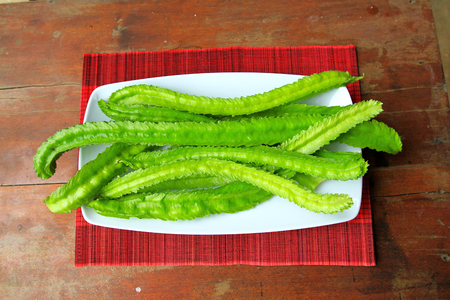 A lot of long winged beans (Psophocarpus tetragonolobus) on wooden table and red mat.の写真素材