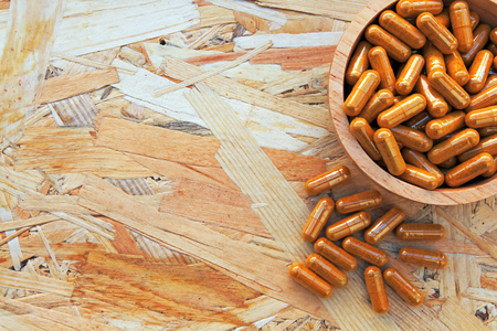 Heap of  yellow pills in the wooden bowl or yellow capsule on the wood background. tablets, healthy, cure, herb and medicine conceptの写真素材