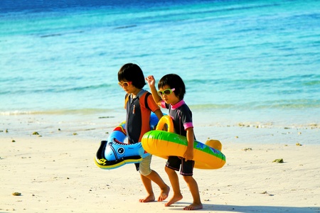 Satun, Thailand - December 16, 2012: Asian twin kids are wearing sunglasses and having fun with fantasy inflatable swimming ring on the tropical beach.Playing, Funny and happiness childrenのeditorial素材