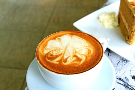 Cup of hot cappuccino coffee on the table with blurred cake and whipped cream backgroundの写真素材