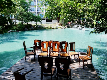 Many wooden chairs on the wooden floor with trees and green or blue lake background.の写真素材