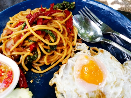 Close up Spaghetti with basil bacon, dried red chili pepper and fried egg with spoon ans fork on the blue plate. Fusion food (Italian and Thai ood) concept. Taste is spicyの写真素材