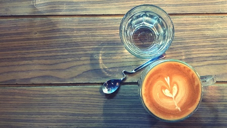 Top view cup of hot art latte coffee and glass of water with beautiful design spoon on wooden table or background with copy space in vintage color style.の写真素材