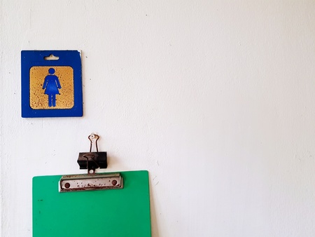 Old blue/gold stainless steel female toilet label and with half green note board hanging on the white wall with copy spaceの写真素材
