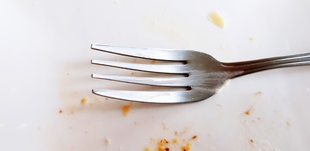 Close up stainless steel fork on dirty white plate or dish after eating dessert or food - Single...