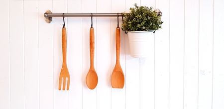Brown wooden fork, spoon, turner or flipper and green plant in white stainless pot hanging and...