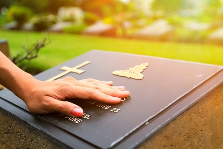 Woman's hand touching the black stone grave at cemetery with orange sunlight flare - Reminisce, Memory, miss, sad and lose person in the family or important people conceptのeditorial素材