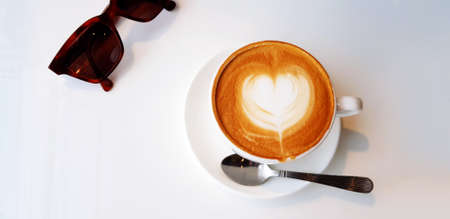 Top up or flat lay of cup of hot art latte coffee or cappuccino coffee and brown sunglasses isolated on white background with copy space. Refreshment drinking at cafe shop in the morning.の写真素材
