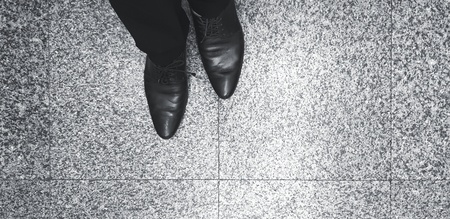 Man's Leg and leather shoes standing on the marble floor in black and white style with copy space -...