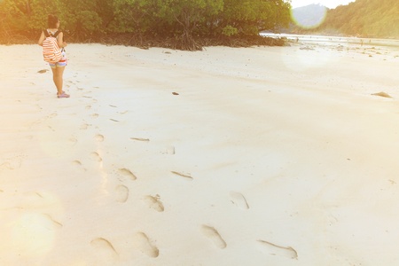 Asian woman backpacker standing on  beautiful white sand beach and looking to sea and mountain with footprint foreground and green trees background with copy space and Orange sun light flare - Touristの写真素材